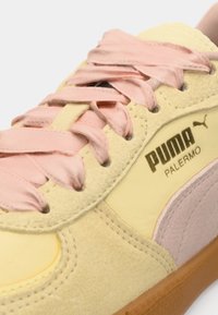 En närbild av en gul och rosa Puma Palermo-sneaker med textillaces och en gummi-sula, som visar sömmar och logotyp på sidan.