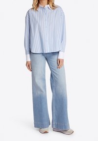 Hellblaus gestreiftes, langärmeliges Hemd mit weißen Manschetten, kombiniert mit weiten, hellblauen Jeans und neutralen Sneakers.