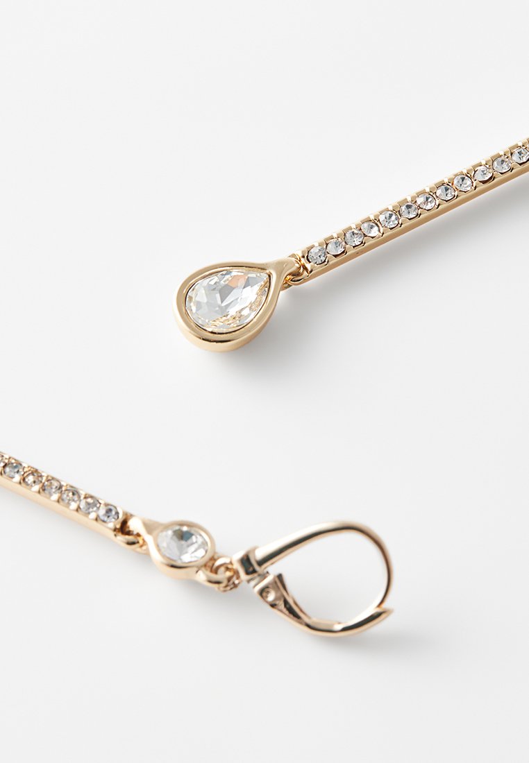 Ohrringe in Goldton zeigen ein lineares Design mit einer Reihe kleiner klarer Kristalle und einem tropfenförmigen klaren Steinakzent.