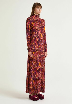 Langes Kleid aus violettem Stoff mit floralen Mustern in Orange- und Pinktönen. Verfügt über einen hohen Kragen und lange Ärmel. Kombiniert mit Plateau-Sandalen.