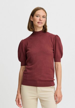 Maglione corto a maniche corte color marsala con collo alto, texture a costine e maniche a palloncino, abbinato a pantaloni chiari.