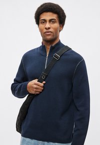 Tengerészkék cipzáros nyakú pulóver kötött anyagból, bordázott gallérral és kontrasztos varrással a vállaknál. Laza szabás.