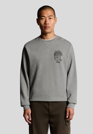 Grå sweatshirt med långa ärmar, rund halsringning och framsides grafikdesign med en karaktär som bär en mössa och texten "HIGHLANDER 1874."