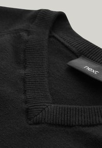 Čierny sveter s výstrihom do V, rebrovaným lemom krku a jemnou textúrou. Obsahuje štítok s názvom značky "next."