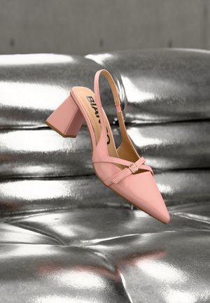 Zapato de tacón slingback rosa con punta puntiaguda, que presenta una correa con hebilla y un tacón triangular grueso. Textura mate suave sobre un fondo metálico.