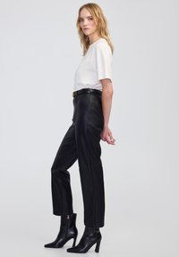 Czarne skórzane spodnie z wysokim stanem i prostymi nogawkami, w połączeniu z białą bluzką z krótkim rękawem i czarnymi botkami na obcasie w kształcie szpicy.