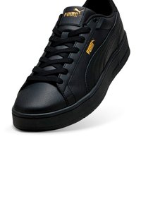 Sneaker in pelle nera con finitura testurizzata, dotato di lacci neri, suola spessa nera e logo Puma dorato sulla linguetta e sul lato.