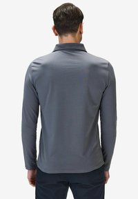 Grå långärmad polotröja med ribbad textur och krage. Rak fåll och subtila sömmar synliga. Minimalistisk design, inga mönster.