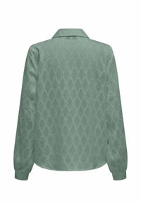 Camicia a maniche lunghe di colore verde chiaro con un motivo a diamante testurizzato, caratterizzata da colletto e orlo leggermente curvo.