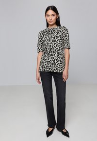 Hnědo-černý vršek s leopardím potiskem a krátkým rukávem, v kombinaci s přiléhavými černými džíny a špičatými černými balerínami, na neutrálním pozadí.