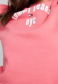 Koralrosa sweatshirt med rund halsringning, "Tommy Jeans NYC" tryckt i vitt och en liten logotypsaccent. Mjuk bomullsmaterial.