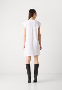 Abito corto bianco in cotone con maniche a cappuccio, vestibilità ampia e scollatura tonda, abbinato a stivali neri in pelle al ginocchio.