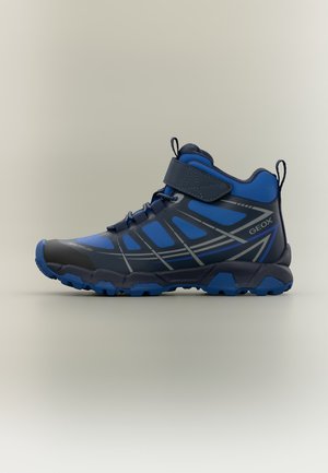 Chaussure de randonnée montante bleue et noire avec bride Velcro, semelle texturée et motif réfléchissant géométrique sur le côté.