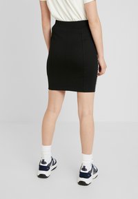Černá přiléhavá mini sukně s vysokým pasem, navržená s zakřivenými švy a kontrastním postranním panelem se textem. Hladký materiál s mírnou pružností.