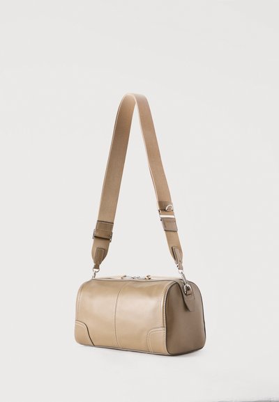 Τσαντάκι από δέρμα σε καφέ χρώμα, ορθογώνιο σχήμα, με ρυθμιζόμενο φάρδος υφασμάτινο ιμάντα ώμου και ασημένιο φερμουάρ, πάνω σε λευκό φόντο.