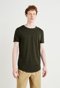 Tricou oliv cu mânecă scurtă, cu guler rotund și tivuri rulate la mâneci, fabricat dintr-un material moale și neted. Design simplu și croială.