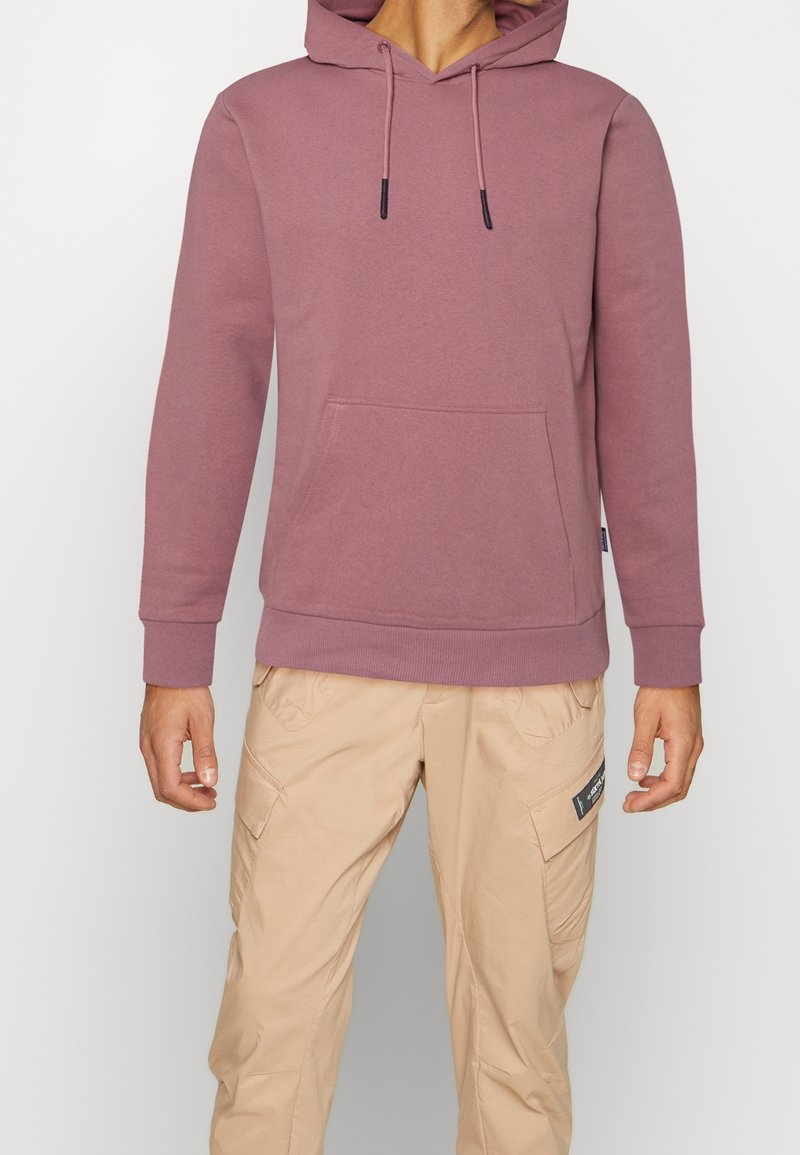 Felpa bordeaux in tessuto felpato con tasca a marsupio, cordini, polsini e orlo a costine; abbinata a pantaloni cargo beige con tasche.