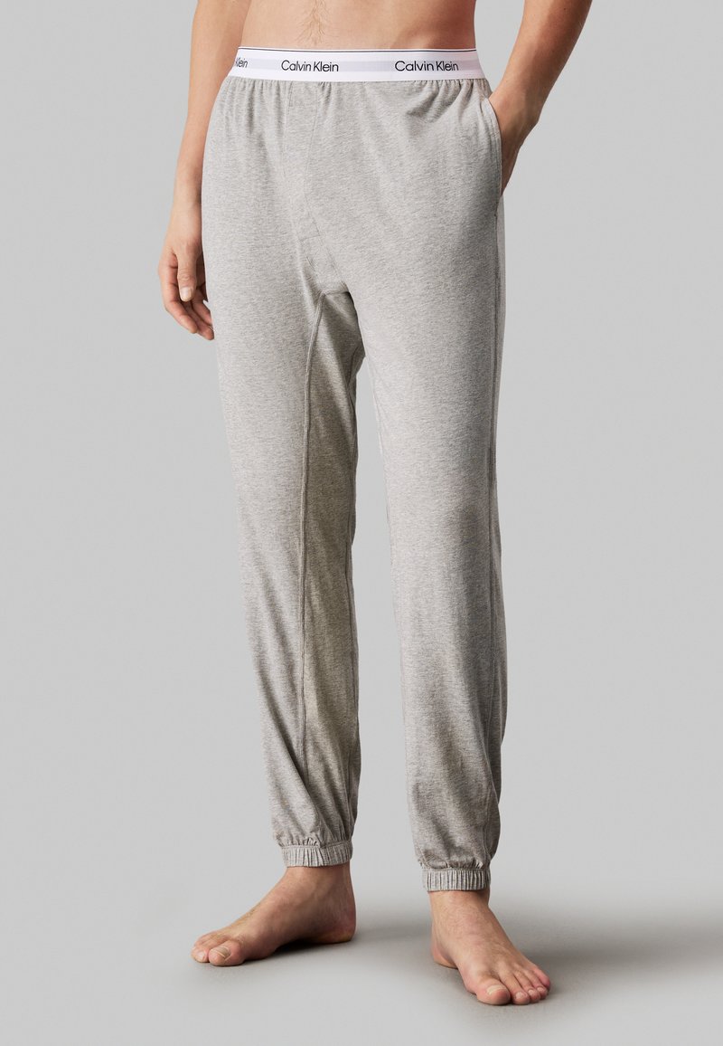 Szürke pamut melegít�őnadrág, elasztikus derékpánttal, "Calvin Klein" logóval, szűkített bokákkal, oldalsó zsebekkel, sima textúrával és laza szabással.