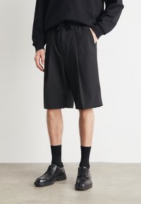 Musta joustovyötäröllä ja nyörillä varustetut shortsit, valmistettu sileästä kankaasta. Yhdistetty mustiin juhlakengisiin ja polvipituisiin sukkiin.