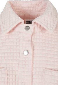 Veste matelassée rose clair avec col pointu et boutons-pression argentés, montrant la texture et les détails des coutures.