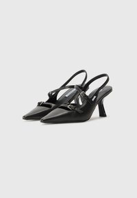 Mustat nahkaiset slingback-korkokengät, joissa on teräväkärkinen muoto, kapeat hihnat, säädettävät soljet ja kohtalainen korko. Sileä pinta kiiltävällä viimeistelyllä.