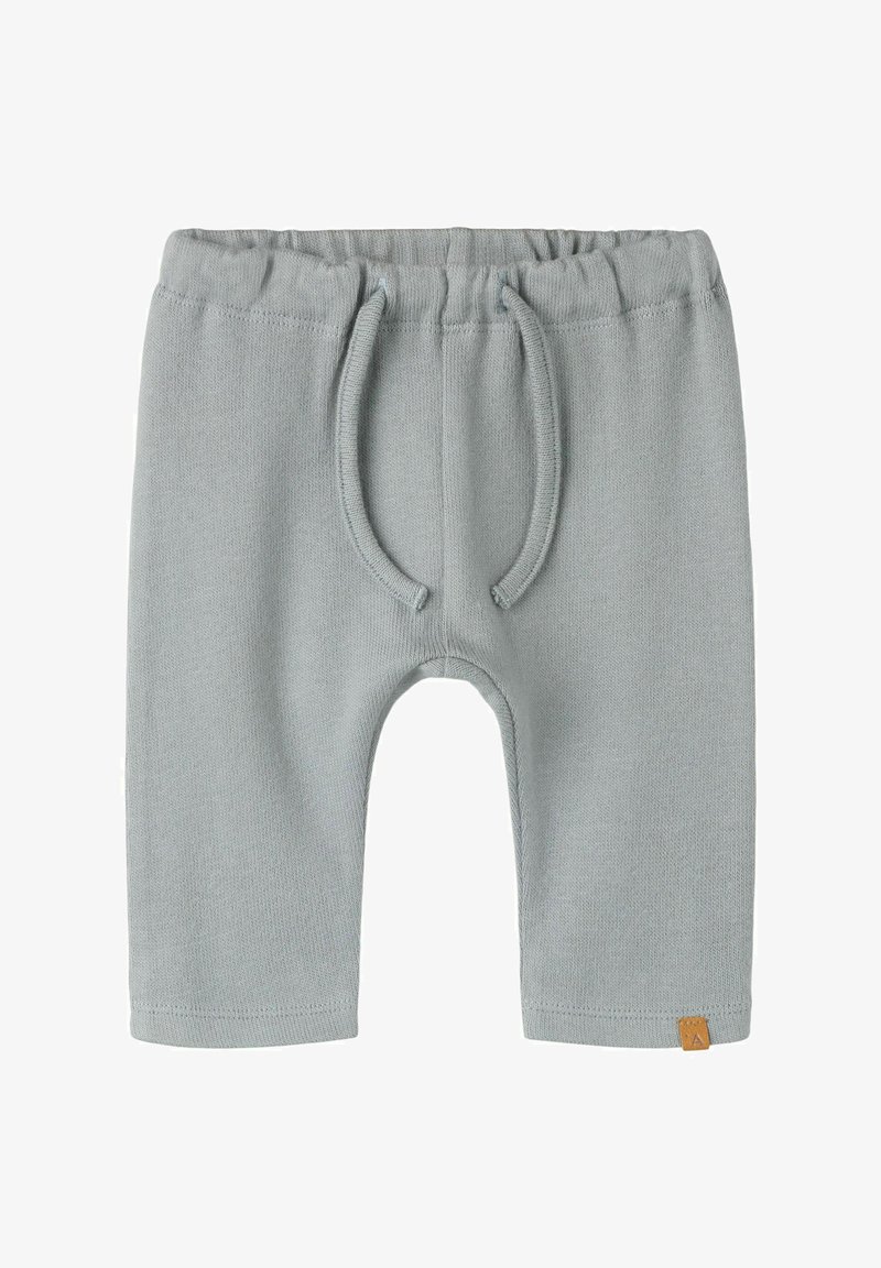 Pantalon bébé tricoté gris clair avec ceinture élastique et cordon, petite étiquette marron sur l'ourlet inférieur, posé à plat sur fond blanc.