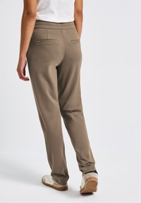 Khakifarbene Sweatpants mit elastischem Bund, zwei Gesäßtaschen und tailliertem Bein Design. Das Material wirkt weich und flexibel.