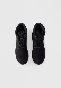 Bottines noires avec un extérieur en cuir lisse, un bout rond et un col rembourré. Comprend des œillets en métal et une semelle en caoutchouc texturée.