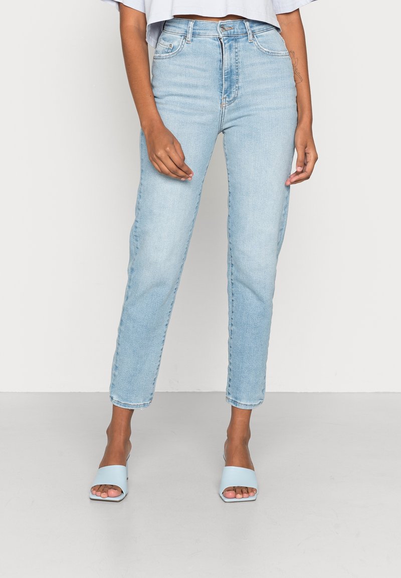 Ljust blå denimjeans med rak passform, femfickorsdesign och lätt urtvättad, i kombination med blåa tofflor.