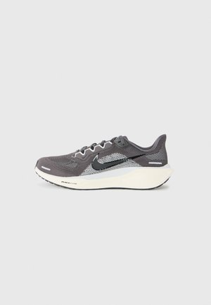 Grå og hvid Nike Air Zoom løbesko med sort swoosh-logo og hvid sål på en simpel lys baggrund.
