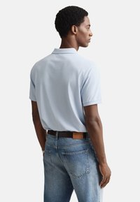 Lichtblauw poloshirt met korte mouwen, gecombineerd met lichtblauwe jeans. Het shirt heeft een klassieke kraag en een gladde textuur.