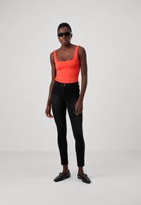 Jasne oranžové tielko bez rukávov, čierne úzke džínsy s vysokým pásom, čierne šmykľavé topánky a tmavé slnečné okuliare. Hladké textúry po celej ploche.