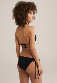 Czarny bikini z fakturowanym topem na szyję z wiązaniami oraz dopasowanymi majtkami z bocznymi wiązaniami, prezentującymi subtelną wzorzystą tkaninę.