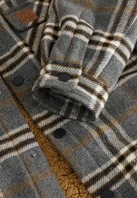 Szara koszula-kurtka w kratę z wełny z pomarańczowymi i białymi akcentami. Posiada czarne zatrzaski i textured fleece podszewkę.
