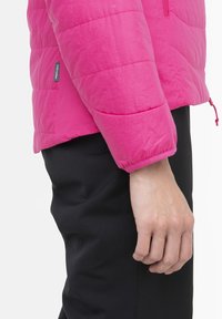 Fuchsiová prošívaná bunda s prošitými panely a černými látkovými kalhotami. Obsahuje elastické manžety a stahovací lem pro nastavitelný fit.