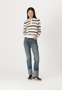 Striped sweater with cream, black, and mauve colors, features a collar and buttons, paired with light blue jeans and black sneakers.