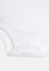 Body en coton blanc pour bébé avec des manches courtes, doté de pressions à la base et de bords côtelés pour une meilleure élasticité.