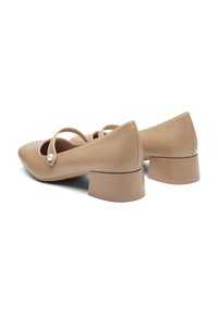 Scarpe in pelle beige con punta affusolata e tacco a blocco. Presentano una fascia con una perla decorativa. Texture liscia con accenti minimi.