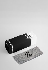 Custodia per occhiali in feltro grigio con patta e logo nero, accanto a una scatola bianca e nera etichettata "ARTIKA". Design minimalista, texture liscia.