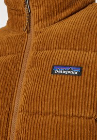 Gilet zip-up in corduroy marrone con colletto alto e texture decorata; presenta un patch del logo Patagonia nero sul davanti.