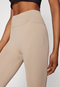 Leggings beige con canalé y cintura alta, con una textura suave y un diseño sin costuras. El primer plano muestra el detalle del patrón de la tela.