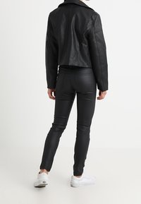 Giacca in pelle nera cropped abbinata a pantaloni skinny neri e sneakers bianche. Texture liscia con dettagli di cucitura nei pantaloni.
