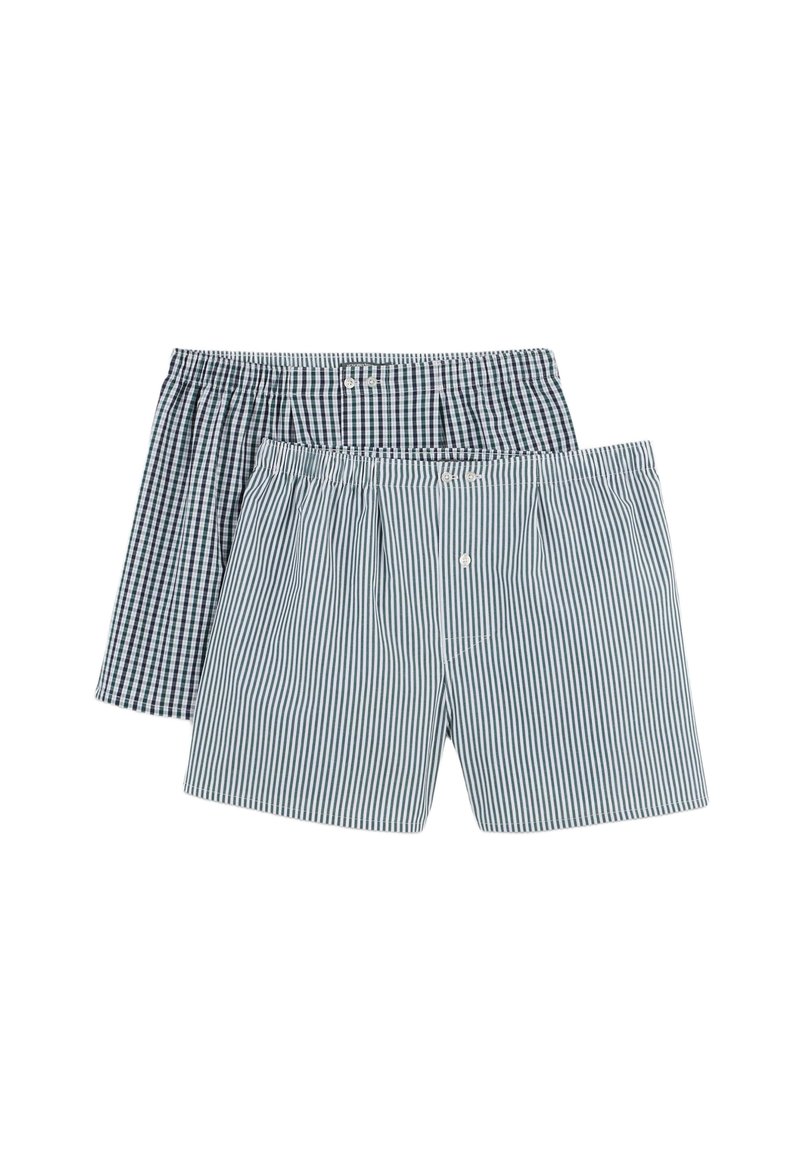 Une paire de boxeurs en tissu coton. L'un a un motif à carreaux sombres, l'autre présente des rayures verticales bleues et blanches. Chacun a un bouton sur le devant.