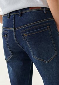 Vaqueros de mezclilla azul oscuro con un diseño ajustado, costuras amarillas en contraste y dos bolsillos traseros con contornos angulados.
