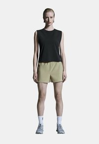 Černý top bez rukávů v kombinaci se světlými béžovými šortkami, které mají elastický pas; model má na sobě šedé sportovní boty a bílé ponožky.