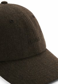 Brown herringbone cap with a curved visor; features embroidered "Hugo" logo on the front. Made from textured fabric, providing a structured look.