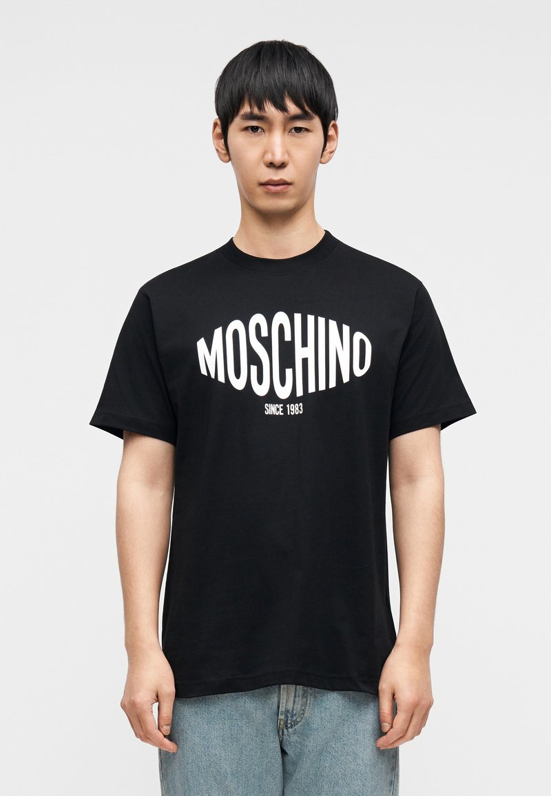 T-shirt en coton noir avec un logo blanc "MOSCHINO" bien visible et le texte "SINCE 1983", manches courtes et col rond.