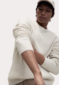 Cremefarbener, gestrickter Pullover mit gerippten Bündchen und rundem Halsausschnitt. Die Textur ist weich mit einem dezenten Karomuster.