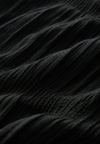 Schwarzer texturierter Stoff mit vertikalen Rillen; weiches und elastisches Material, das ein wellenförmiges Muster über die Oberfläche erzeugt.