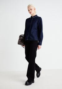 Dark denim shirt with a fitted design and metallic button details at the collar; paired with black flared pants and platform shoes.